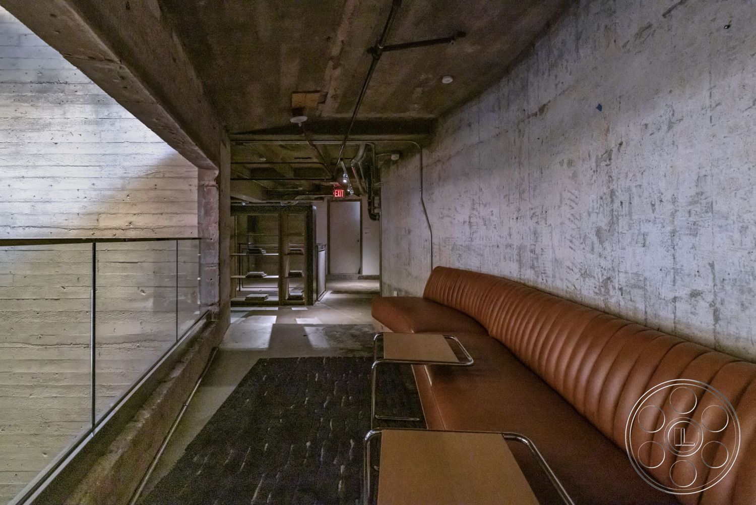 Sunset Campus - glass railing, exposed concrete walls, concrete ceiling, dark flooring, industrial aesthetic, modern architectural details, minimalist design interior, leather upholstered seating