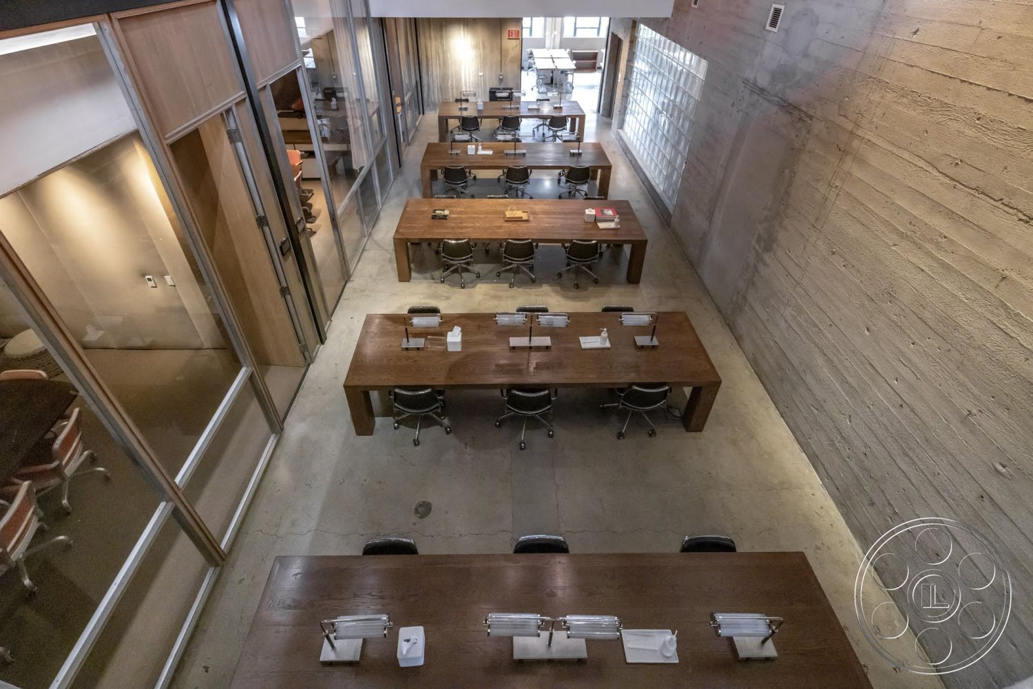 Sunset Campus - minimalist decor, natural light, concrete floor, exposed concrete walls, collaborative workspace, floor-to-ceiling windows, open office layout, glass partition walls, metal office chairs, modern industrial style, bright lighting fixtures, large wooden conference tables