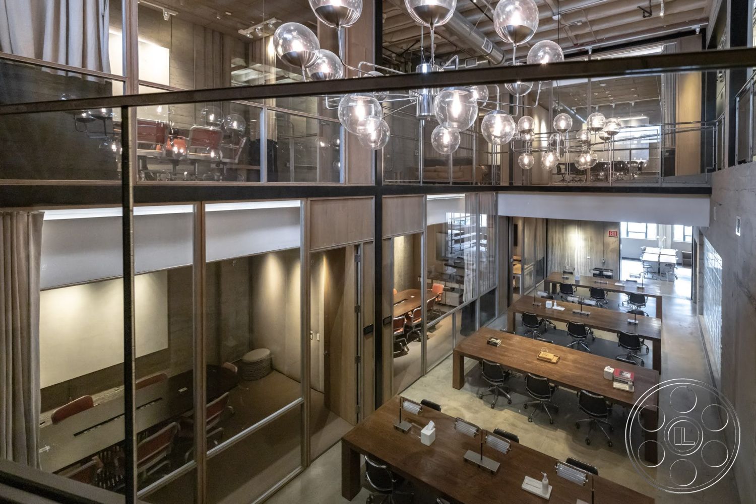 Sunset Campus - concrete flooring, exposed concrete walls, collaborative workspace, floor-to-ceiling windows, black office chairs, open office layout, glass partition walls, textured plaster wall, wood beam ceiling, modern chandelier lighting, long wooden conference table, workstations with desks