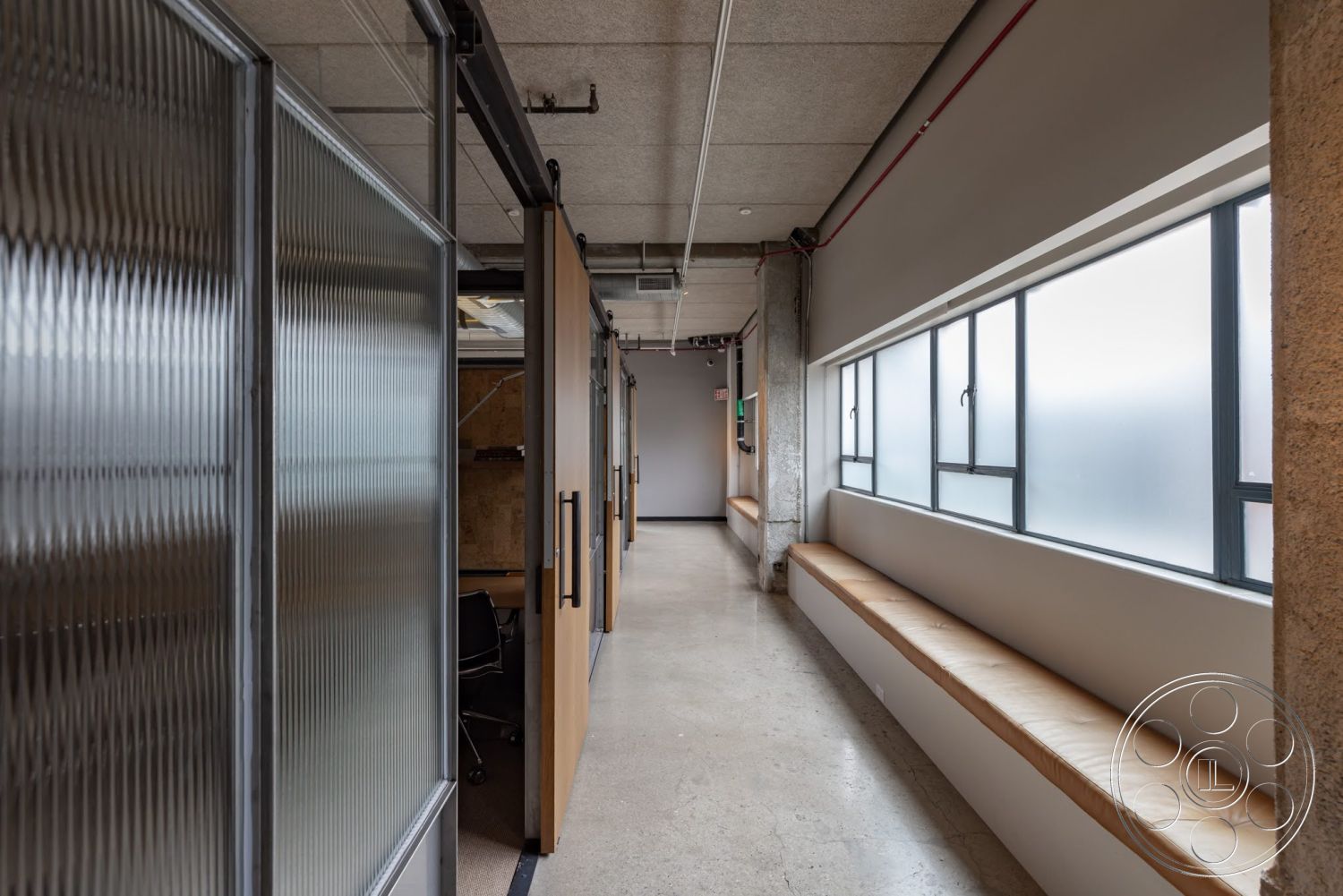 Sunset Campus - neutral color palette, large windows, concrete flooring, exposed concrete walls, industrial style, wooden bench seating, metal framing, glass partition walls, modern office space, open corridor design, rectangular office layouts