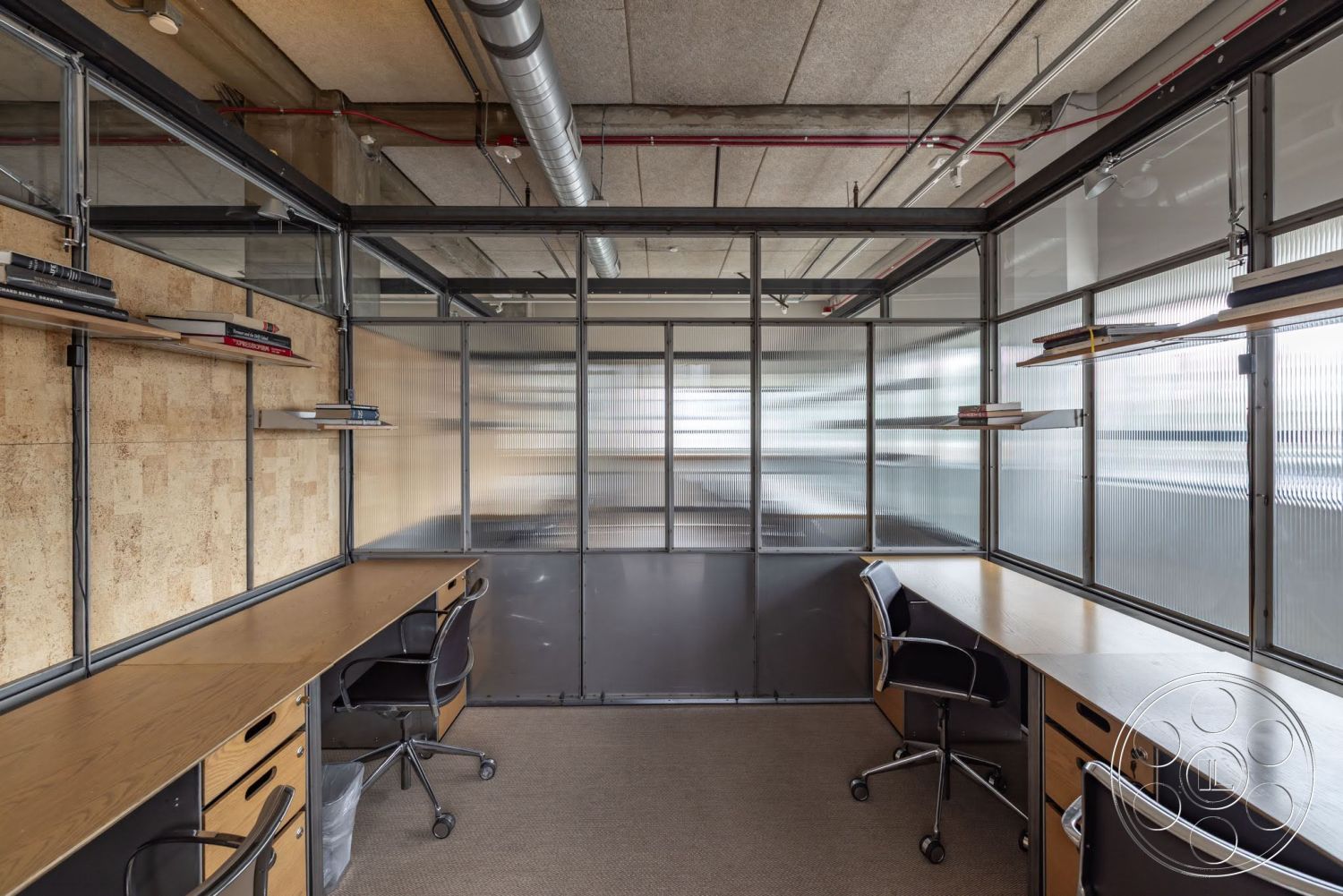 Sunset Campus - suspended lighting fixtures, exposed concrete ceiling, glass partition walls, modern office design, minimalist workspace, carpeted office flooring, double glass doors, steel framing details, wood desktop, cork wall finish, shelving units with books