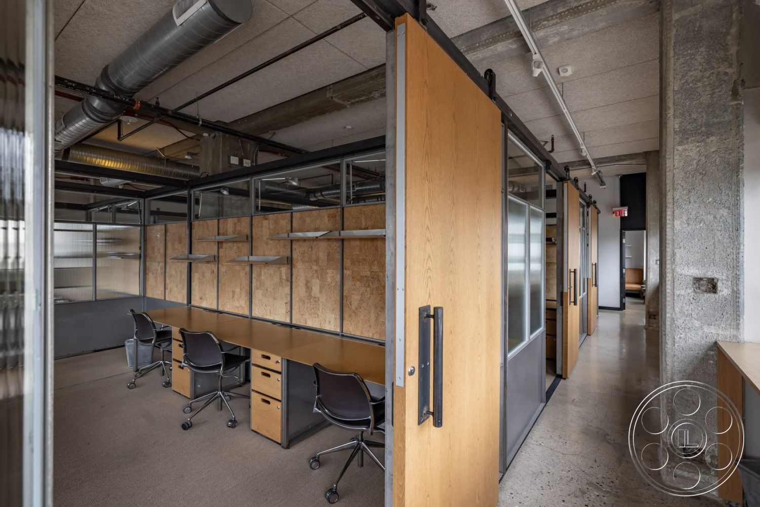 Sunset Campus - concrete floor, exposed concrete walls, suspended lighting fixtures, black office chairs, open office layout, modern office space, wooden desk surfaces, plywood wall panels, industrial ceiling with exposed ducts, wood sliding doors, metal frame glass partitions