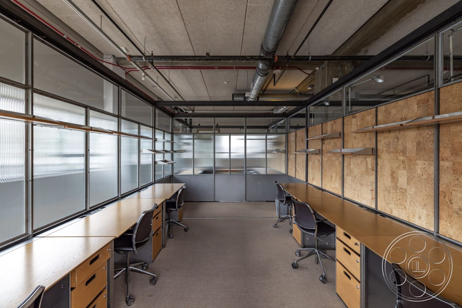 Sunset Campus - suspended lighting fixtures, exposed ductwork, concrete ceiling, glass partition walls, textured carpet flooring, wooden desk surfaces, cork wall treatment, black metal drawer units