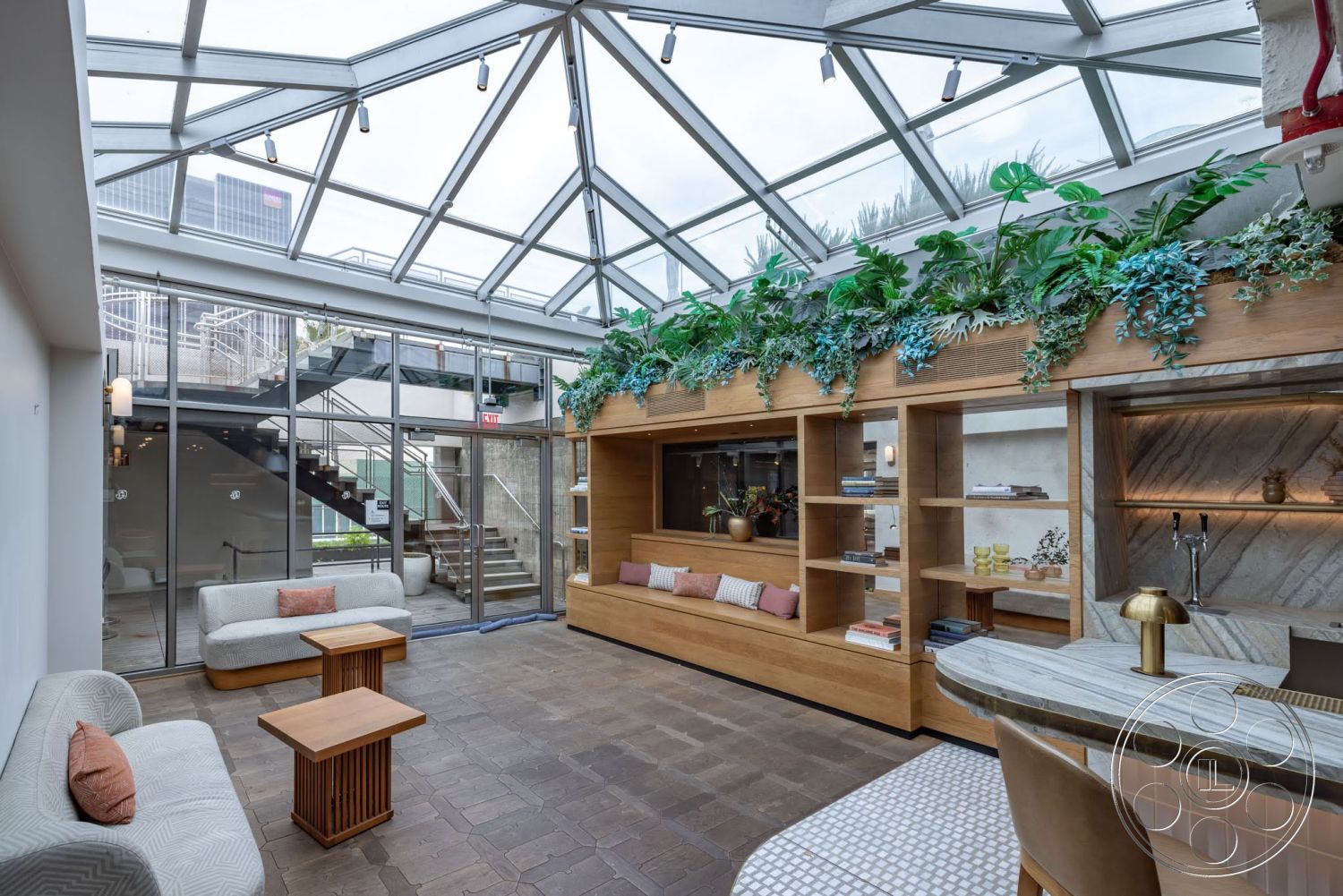 Sunset Campus - open floor plan, modern pendant lighting, ceramic tile flooring, planted greenery, wood accent wall, light wood shelving, textured stone backsplash, minimalist design aesthetic, upholstered accent chairs, glass roof skylight, natural stone bar countertop, metal staircase railing