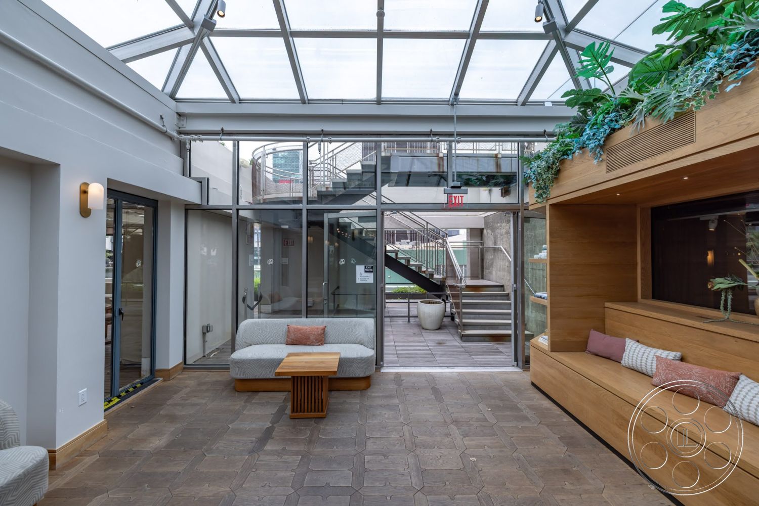 Sunset Campus - plant decor, stone flooring, modern coffee table, floor-to-ceiling windows, glass ceiling, vaulted ceiling, wooden bench seating, textured plaster walls, exposed steel stair railing, airy atrium