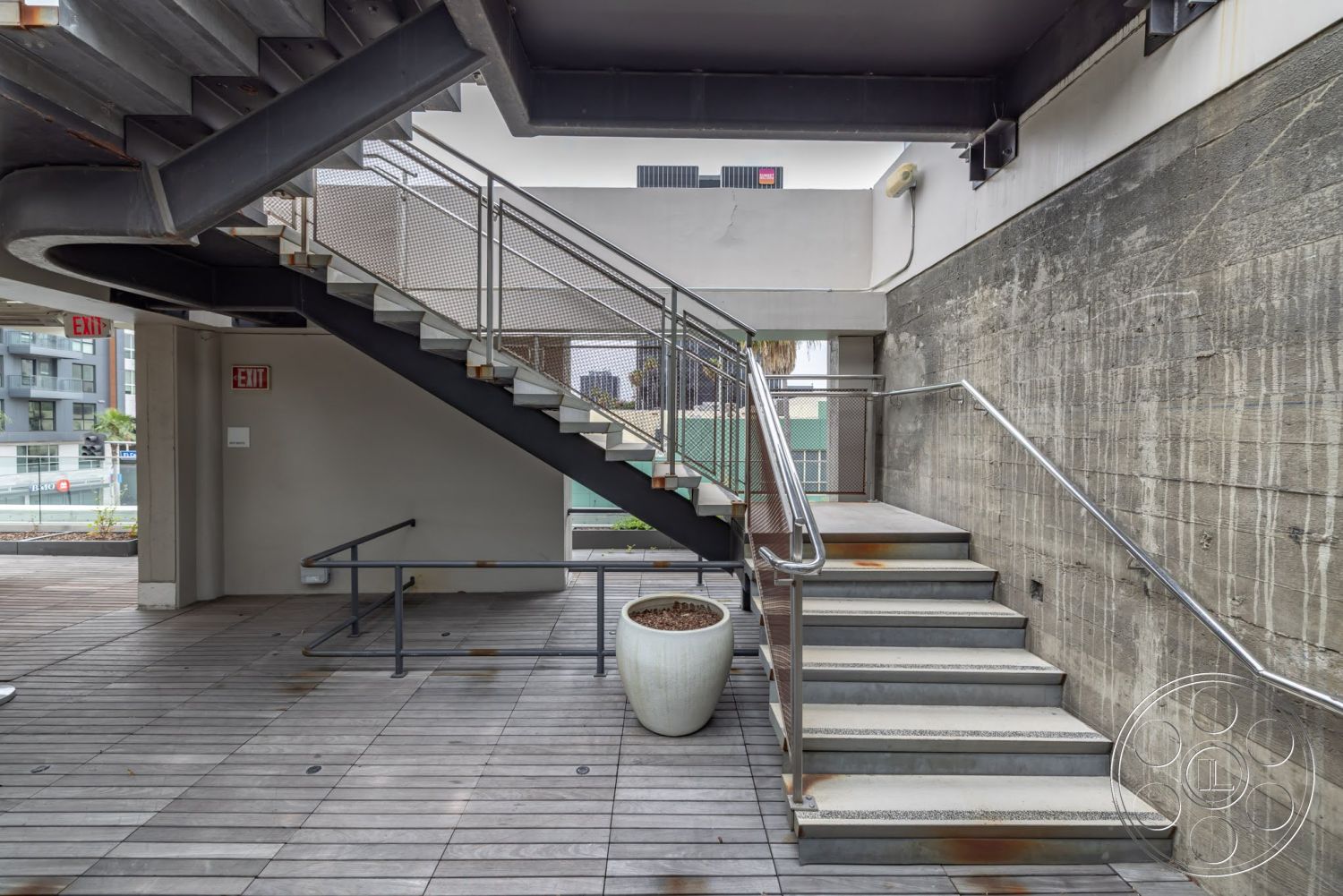 Sunset Campus - exterior, exposed concrete walls, urban setting, floor-to-ceiling windows, planter pot, curved staircase, concrete retaining wall, wooden deck flooring, modern architectural design, metal stair railings, concrete staircase