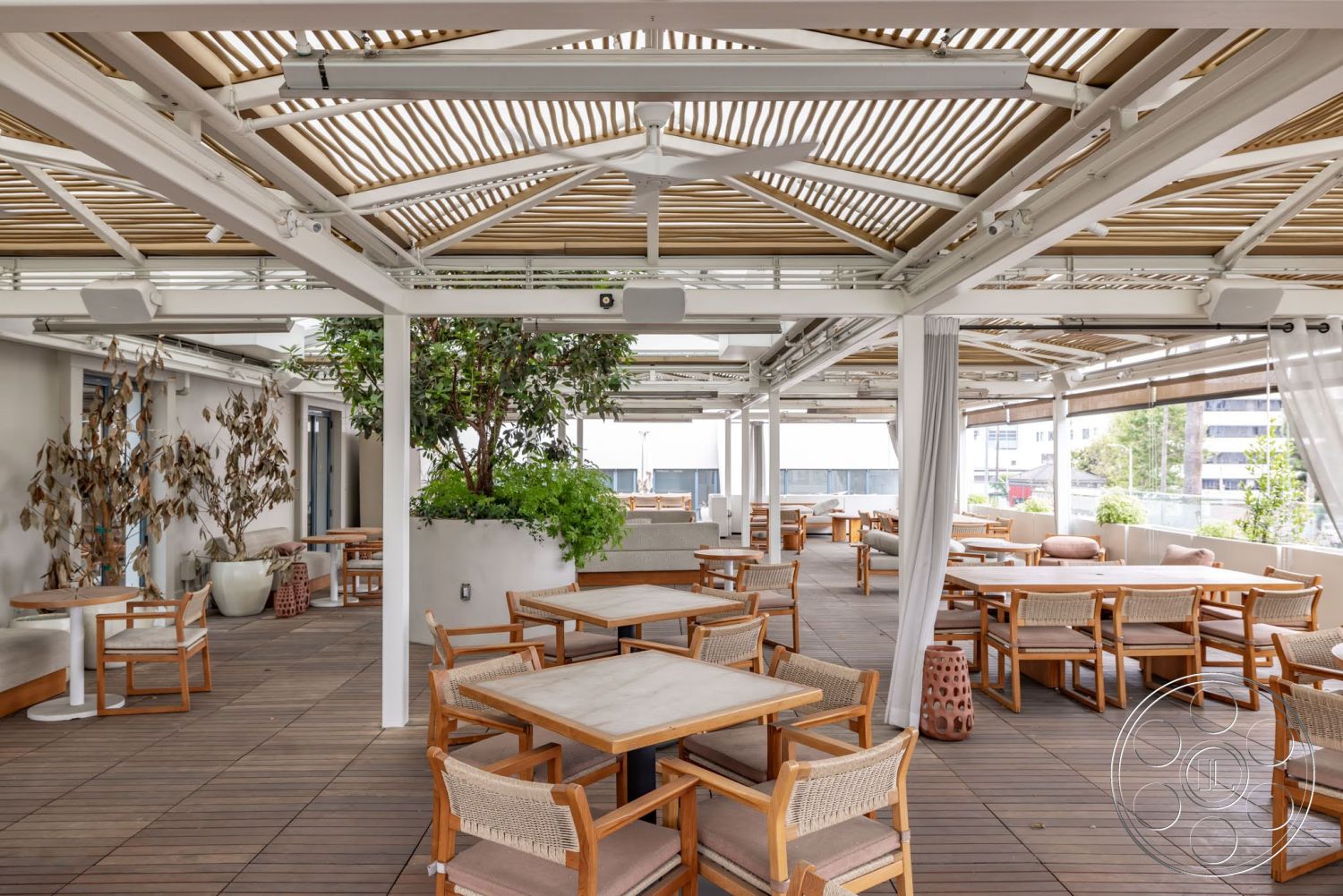 Sunset Campus - exterior, landscaped greenery, modern architectural style, woven outdoor chairs, concrete floor tiles, wooden slatted roof, freestanding white planters, outdoor wooden dining tables, open air café