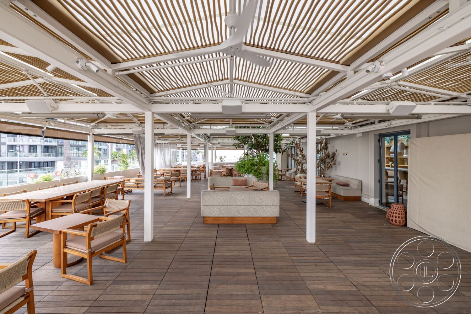 Sunset Campus - exterior, glass sliding doors, outdoor seating area, wooden deck flooring, modern architectural design, urban rooftop setting, greenery indoor plants, aluminum pergola structure, composite dining tables, woven fabric lounge seating, vertical wood slats canopy