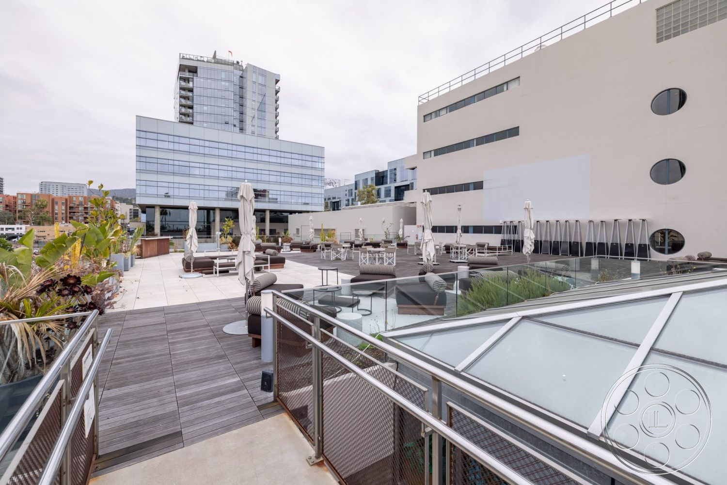 Sunset Campus - exterior, metal railings, modern architectural style, concrete terrace flooring, surrounding urban setting, wooden decking area, glass sunroof, outdoor lounge furniture, poolside umbrellas, extensive plant landscaping