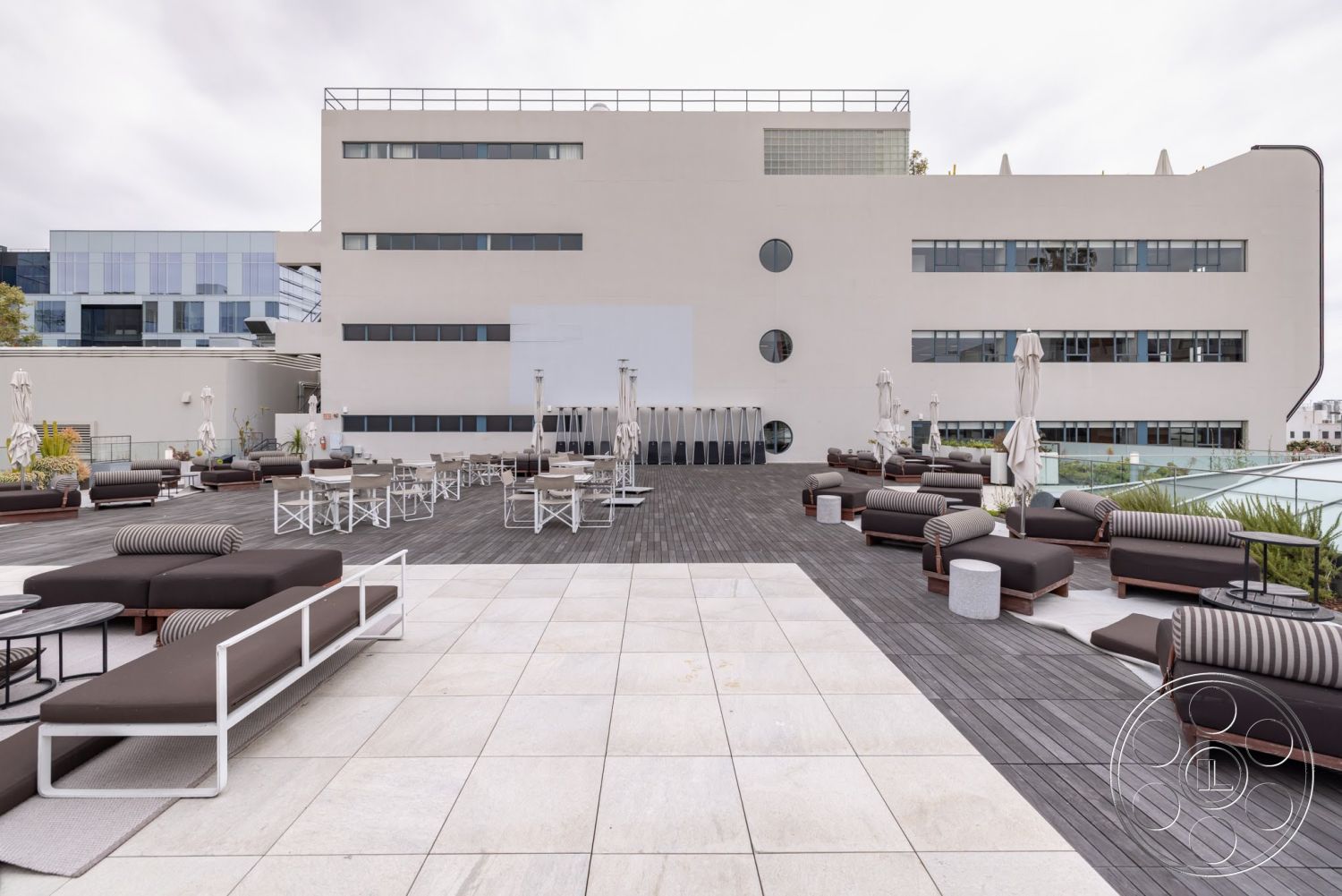 Sunset Campus - large windows, exterior, glass railing, wood deck, rectangular layout, flat roof design, contemporary architectural style, concrete patio flooring, modern lounge seating, planter boxes with greenery, folding umbrellas