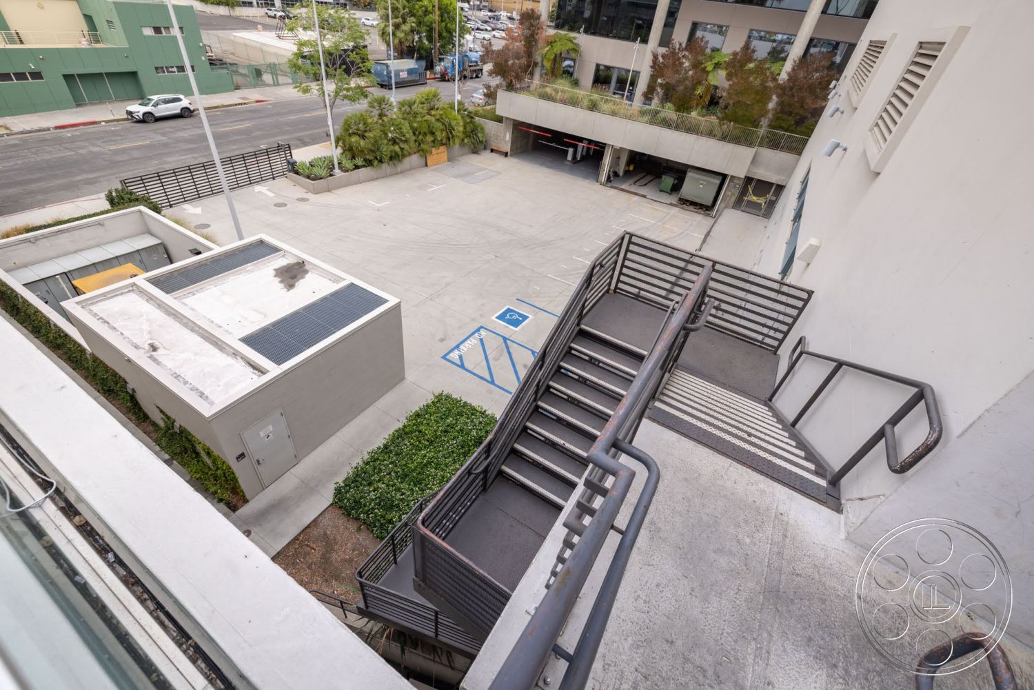 Sunset Campus - exterior, landscaped greenery, stone pavers, planting beds, concrete parking lot, metal staircase, solar panel roof, urban courtyard setting, steel stair railings, modern commercial building
