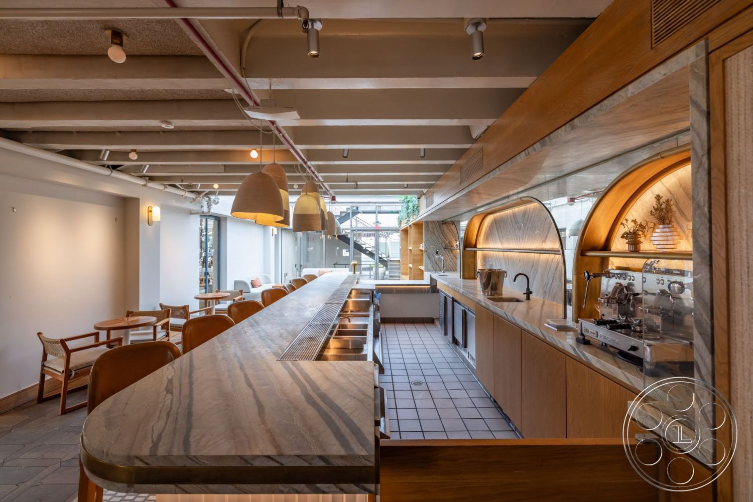 Sunset Campus - large windows, tile flooring, wood cabinetry, seating area, marble countertop, exposed ceiling beams, pendant lighting fixtures, decorative wall shelves, open kitchen layout, kitchen workspace, light wood bar stools, coffee brewing area