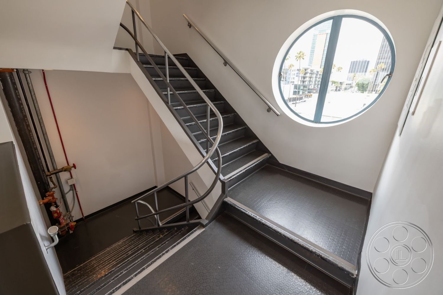 Sunset Campus - circular window, smooth white walls, exposed piping, modern industrial design, metal stair railings, floor-to-ceiling window view, interior staircase, rectangular stair design, rubber stair treads