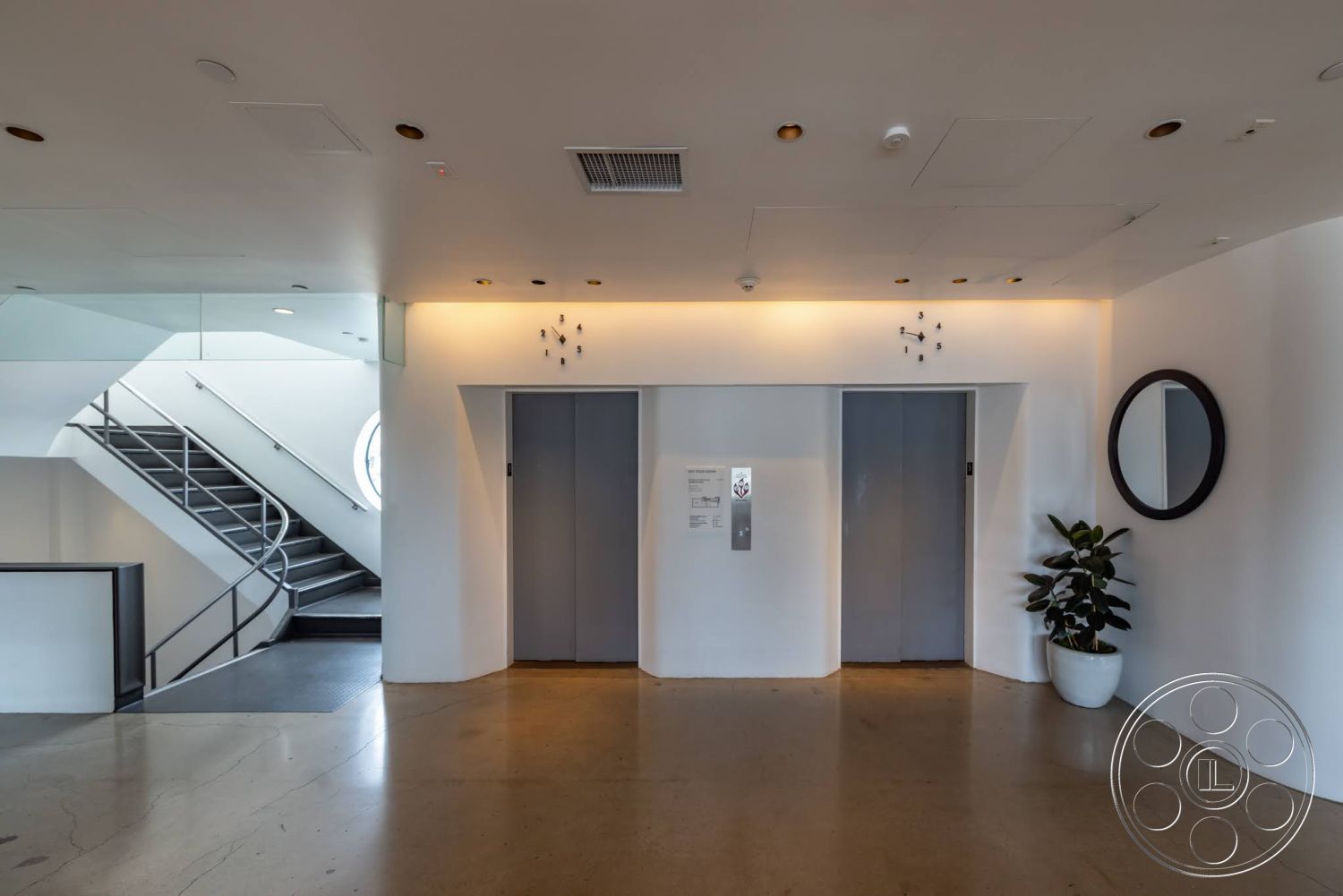 Sunset Campus - polished concrete flooring, circular mirror, glass railing staircase, white painted walls, indoor potted plant, modern elevator doors, wall-mounted clock, rounded doorway frames
