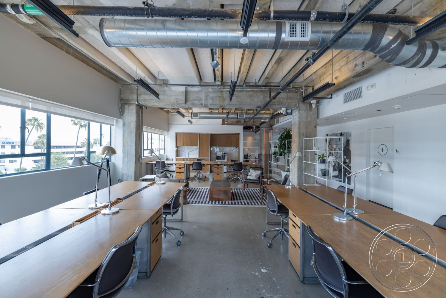 Sunset Campus - natural light, plant accents, polished concrete flooring, concrete walls, task lighting, exposed concrete ceiling, glass partition walls, large windows with city view, minimalist office decor, open workspace layout, wooden office desks, metal ductwork ceiling, industrial style office, modular office chairs