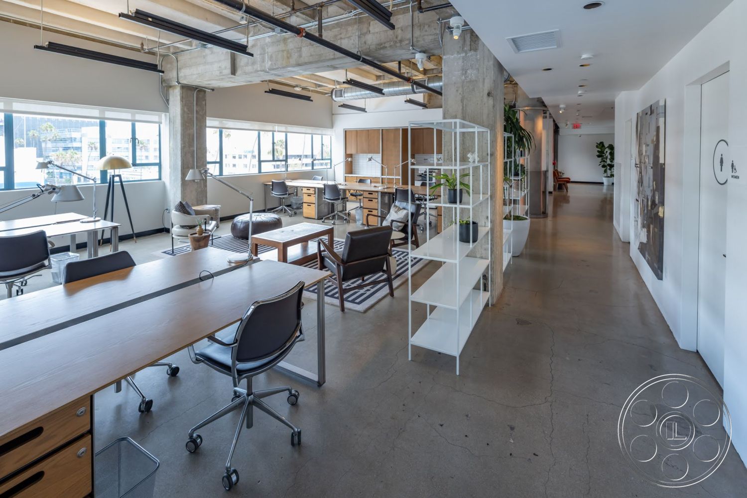 Sunset Campus - minimalist decor, neutral color palette, concrete flooring, exposed concrete walls, modern coffee table, open office layout, interior office space, large windows with city view, potted plants as decor, industrial ceiling beams, steel lighting fixtures, office chairs with wheels, wood desks with storage, glass partition shelves, corridor with white walls