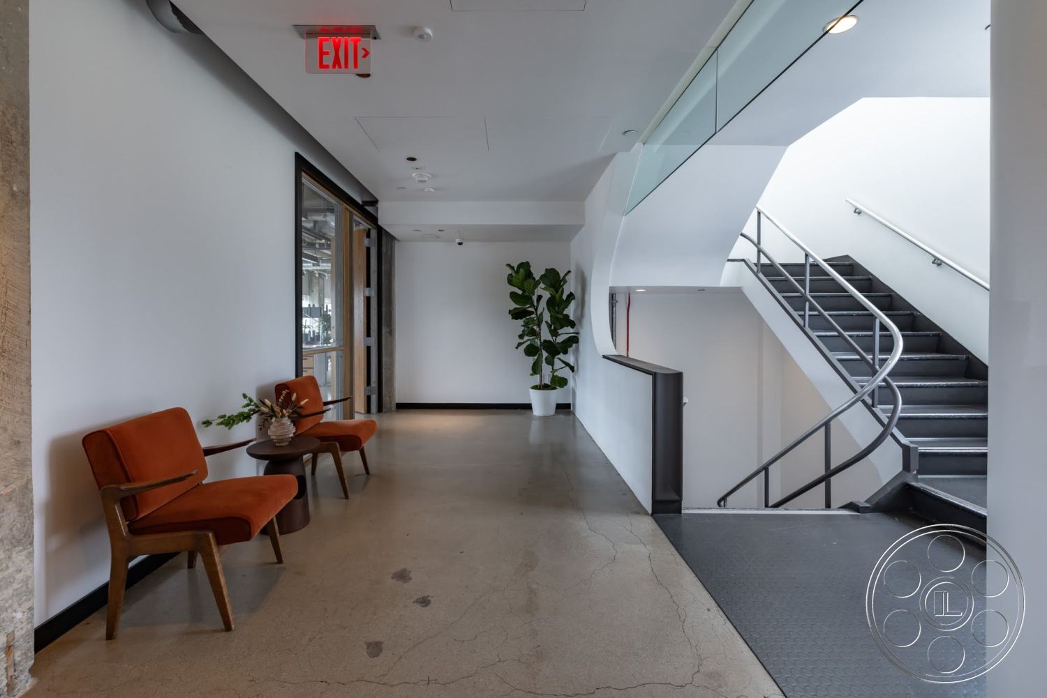 Sunset Campus - modern furniture, polished concrete flooring, glass railing, natural light from large windows, curved staircase, white painted walls, industrial style design, potted indoor plant, steel stair railing, orange upholstered chairs