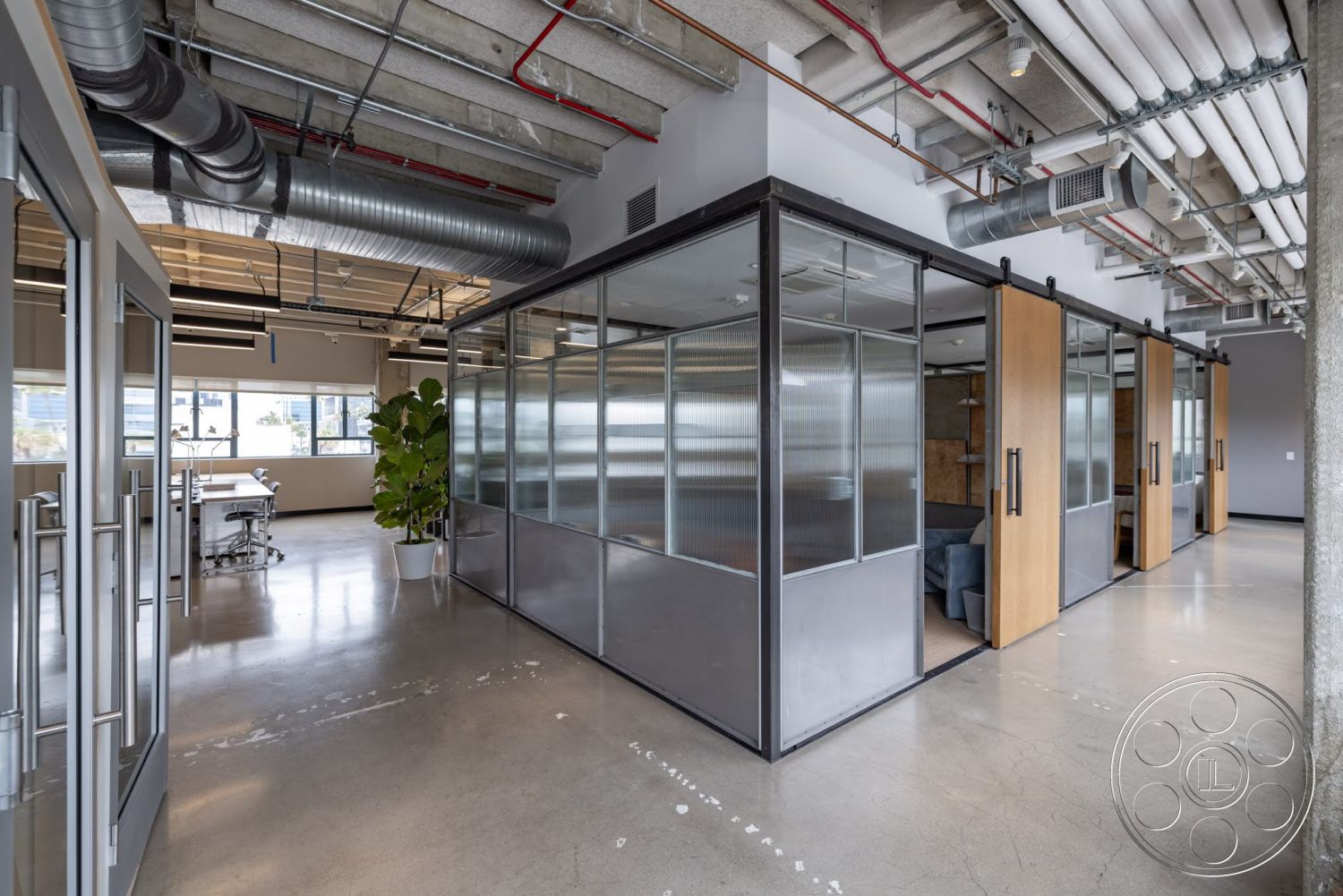 Sunset Campus - industrial lighting fixtures, wooden sliding doors, glass partition walls, potted indoor plants, modern office layout, glass office doors, contemporary workspace, exposed concrete floors, metal frame construction, open ceiling ductwork