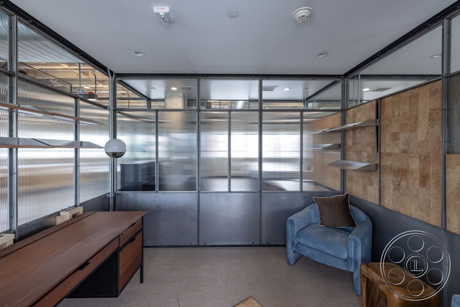 Sunset Campus - modern lighting fixtures, carpeted flooring, steel frame partition walls, corrugated glass office walls, engineered wood desk, textured cork wall panels, suspended glass shelves, plush blue accent chair, natural wood side table