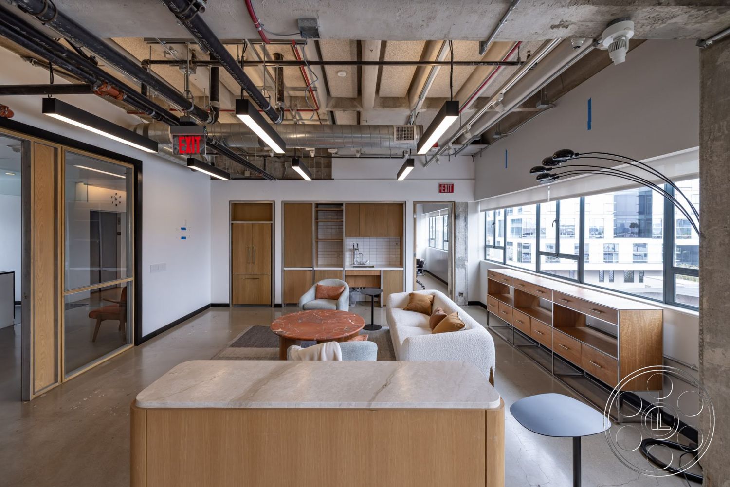 Sunset Campus - minimalist decor, round coffee table, open floor plan, wood cabinetry, concrete floor, modern design elements, textured wall finish, light wood accents, exposed ductwork, natural light from windows, integrated storage solutions, metal light fixtures, glass partition walls, soft seating area