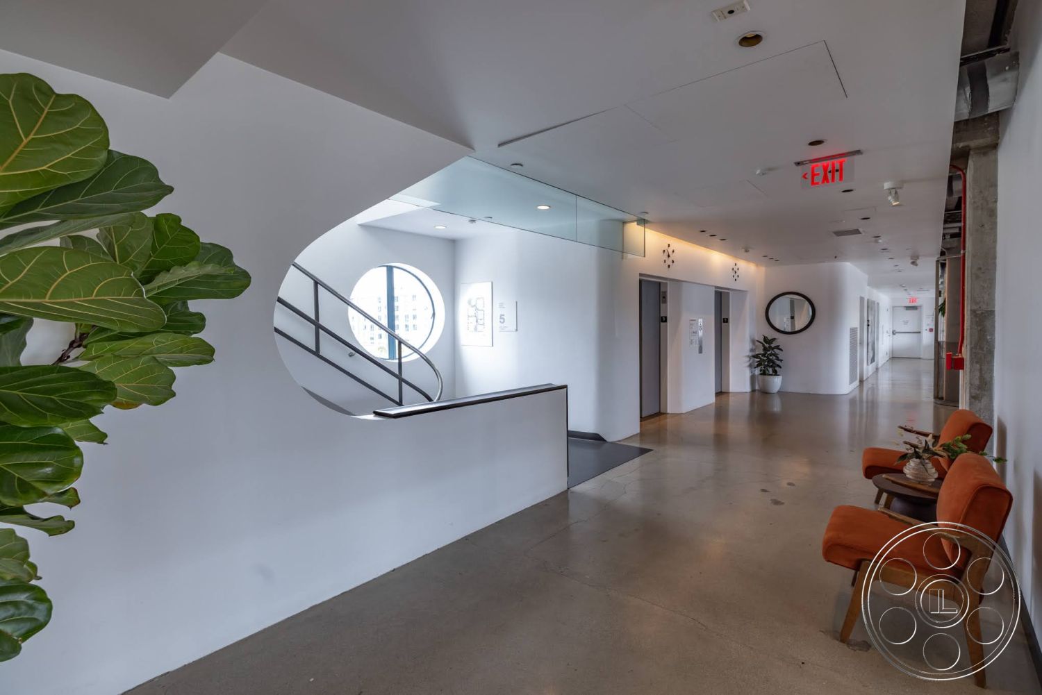Sunset Campus - polished concrete floor, plant decor, glass railings, modern seating area, flush ceiling lights, structural columns, white painted walls, round window opening, exit sign detail