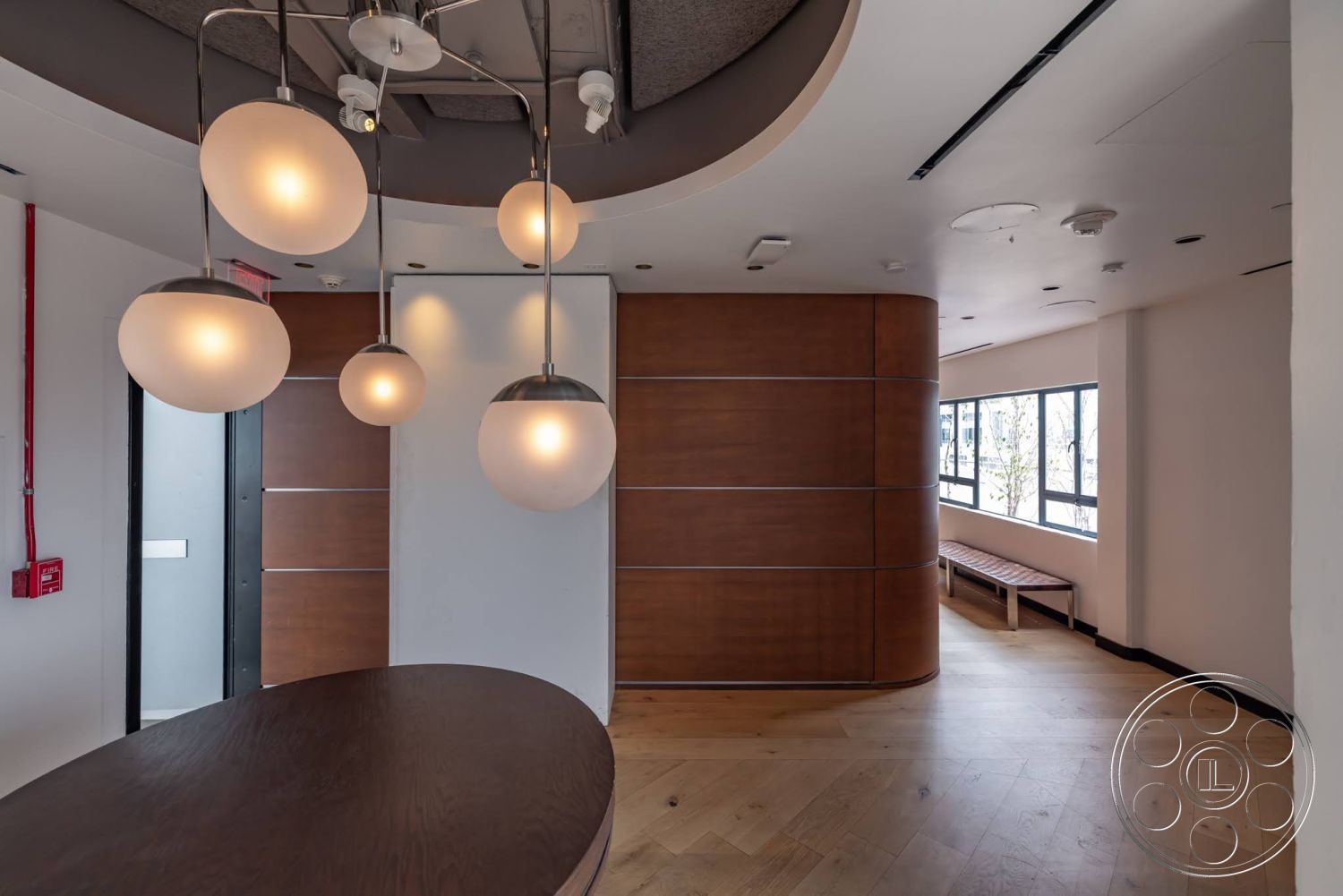 Sunset Campus - minimalist design, open floor plan, modern pendant lighting, floor-to-ceiling windows, polished hardwood flooring, light-colored painted walls, suspended globe light fixtures, curved wooden feature wall, built-in wooden bench