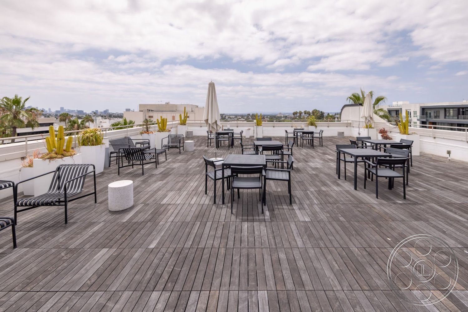 Sunset Campus - exterior, contemporary design, potted plants, city skyline view, open-air patio, wooden deck flooring, black metal outdoor furniture, modern outdoor seating area, urban rooftop setting, umbrella for shade, rectangular dining tables
