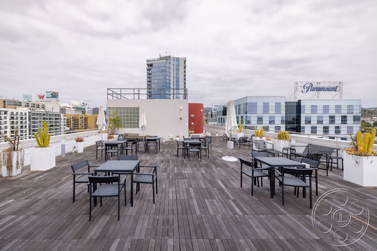 Sunset Campus - exterior, contemporary outdoor furniture, urban skyline view, circular planters, pergola shade structure, wood deck flooring, flat rooftop terrace, high-rise building backdrop, metal dining tables, planter boxes with cacti, cityscape environment