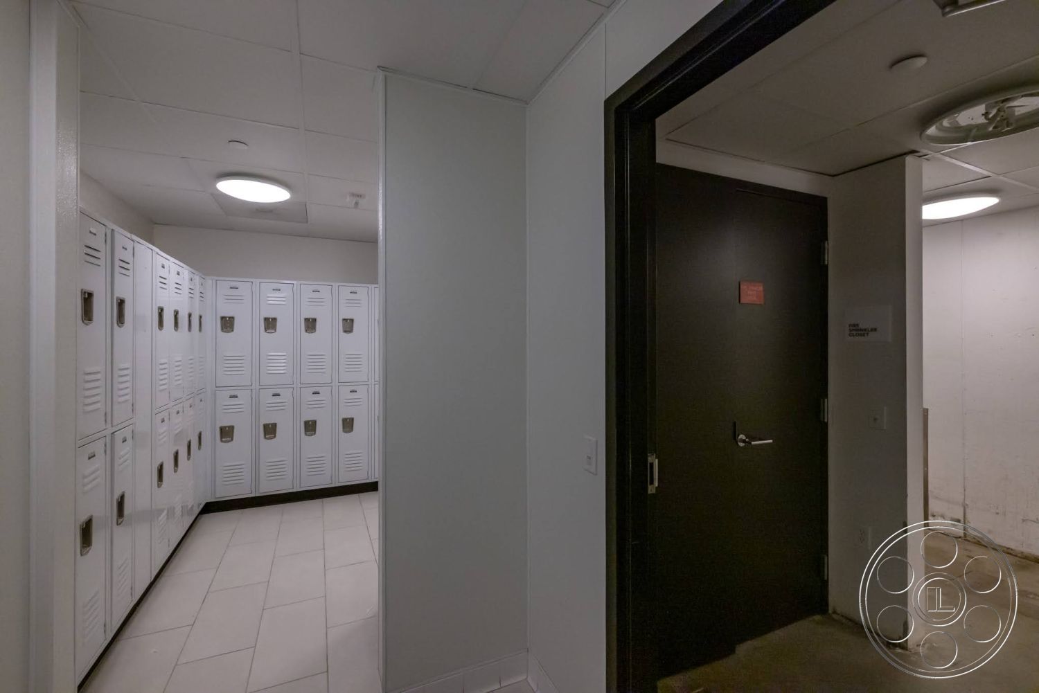 Sunset Campus - neutral color palette, tile flooring, circular ceiling light, smooth plaster walls, black metal door, white metal lockers, indoor changing area
