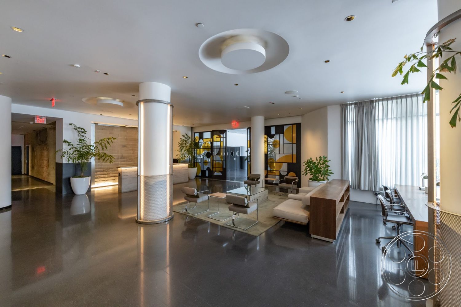 Sunset Campus - indoor plants, open floor plan, polished concrete flooring, glass coffee table, glass sliding doors, exposed ceiling, contemporary light fixtures, white painted walls, modern lounge seating, functional workspace area, large windows with sheer curtains, textured wall accent, metal column, custom wooden reception desk