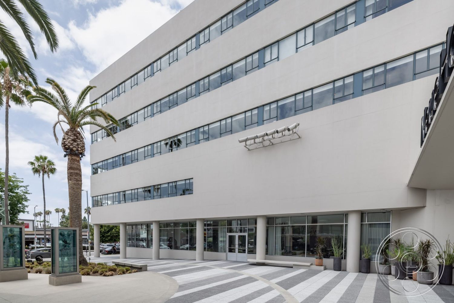 Sunset Campus - exterior, urban setting, concrete planters, modern architectural style, large floor-to-ceiling windows, surrounding palm trees, rectangular building shape, smooth stucco facade, checkered stone walkway