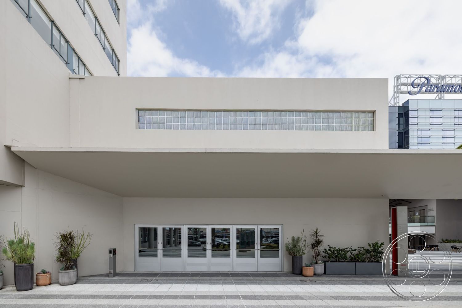 Sunset Campus - exterior, flat roof, minimalist aesthetic, modern design, concrete facade, paved concrete walkway, glass block window, double glass entry doors, large planters, simple linear architecture, horizontal orientation