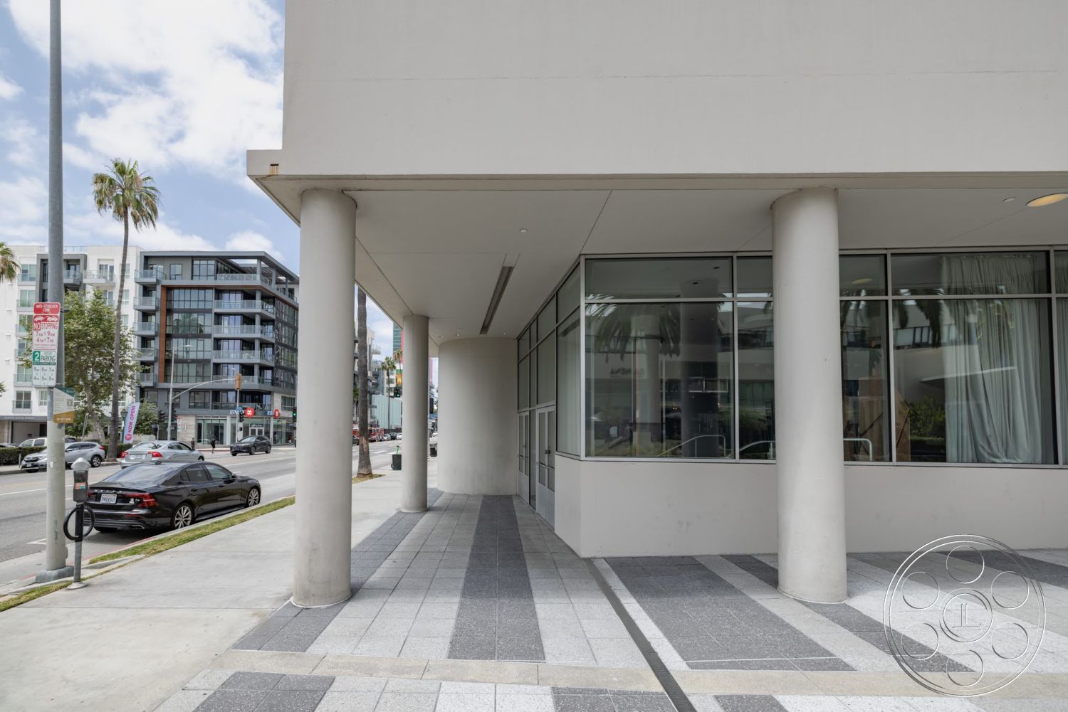 Sunset Campus - exterior, modern architectural style, concrete columns, city street view, glass storefront windows, textured stone paving, palm trees in urban setting, overhanging roof, organized pedestrian walkway, sloping sidewalk