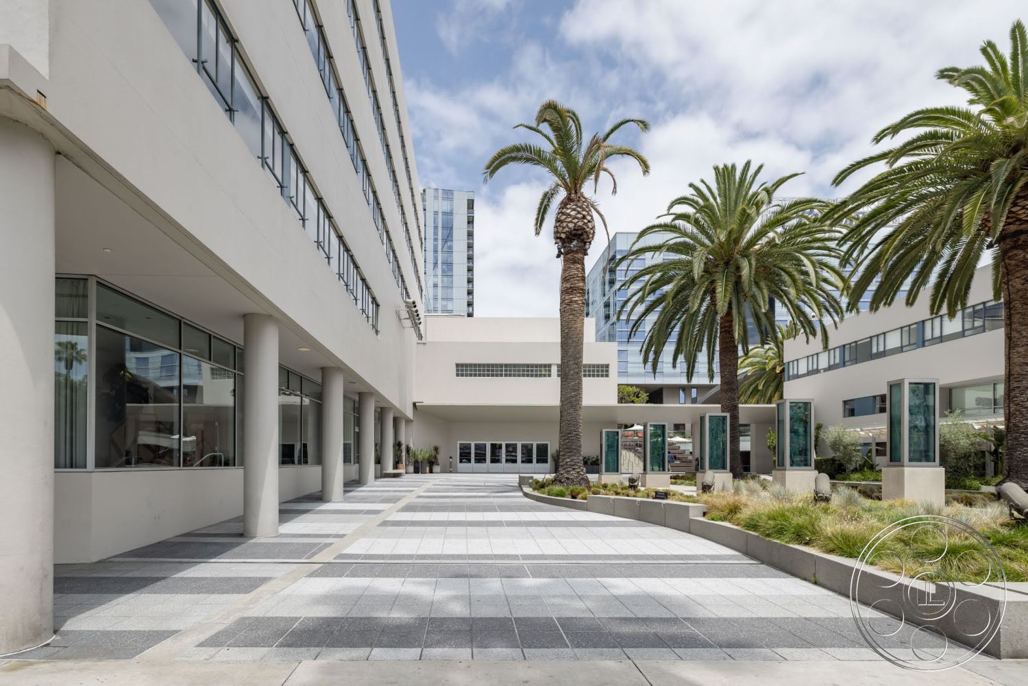 Sunset Campus - exterior, large glass windows, urban setting, modern architectural style, concrete walkway, flat roof structure, palm trees landscaping, commercial building facade, pedestrian-friendly outdoor space, paved plaza with geometric patterns, stainless steel art installations, textured concrete planter boxes