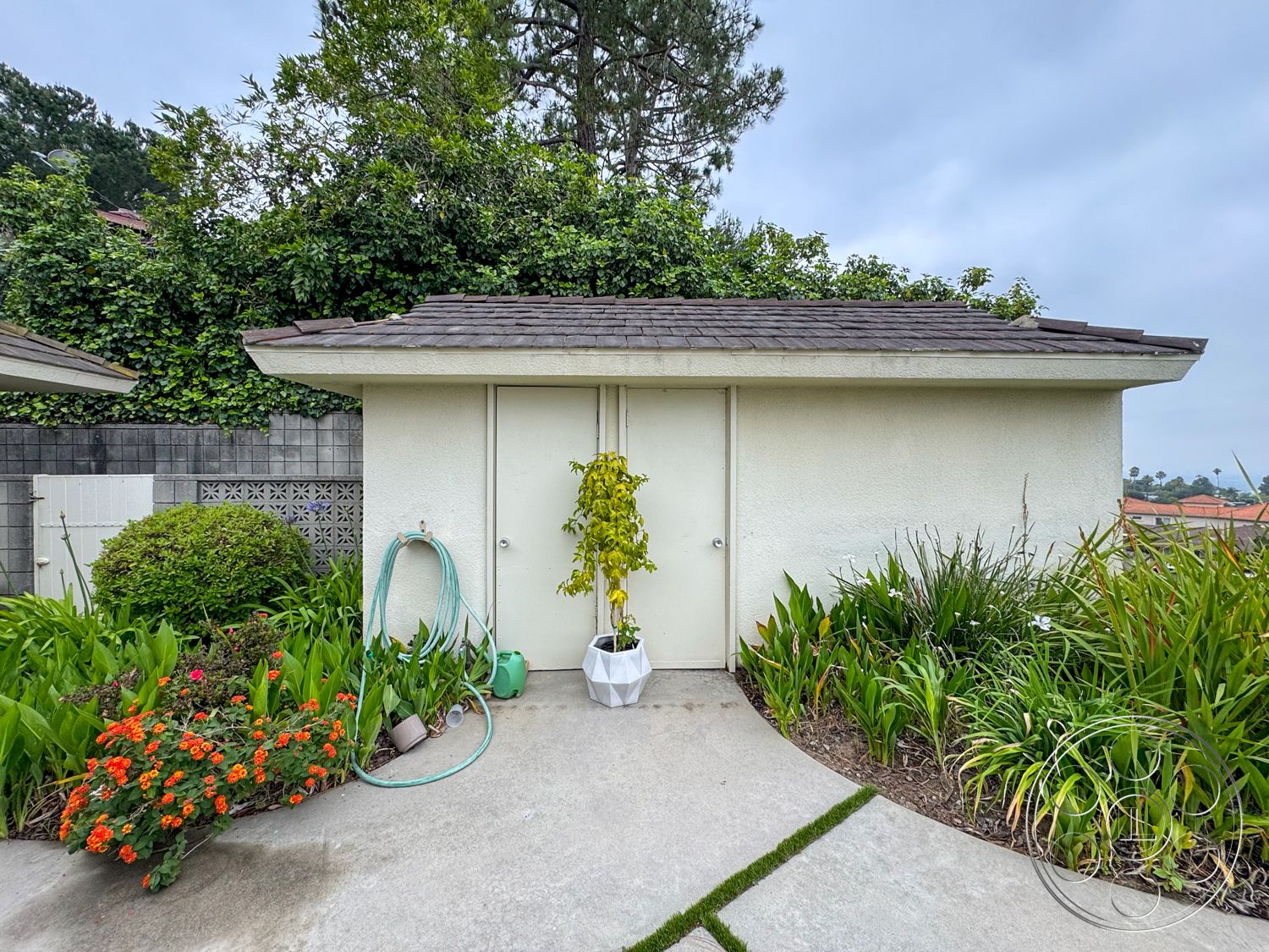 Once Upon Hollywood - exterior, landscaped garden, wooden door, concrete pathway, sloped roof, stucco walls, ornamental shrubbery, flowerbed with orange flowers, green garden hose, indoor garden planter