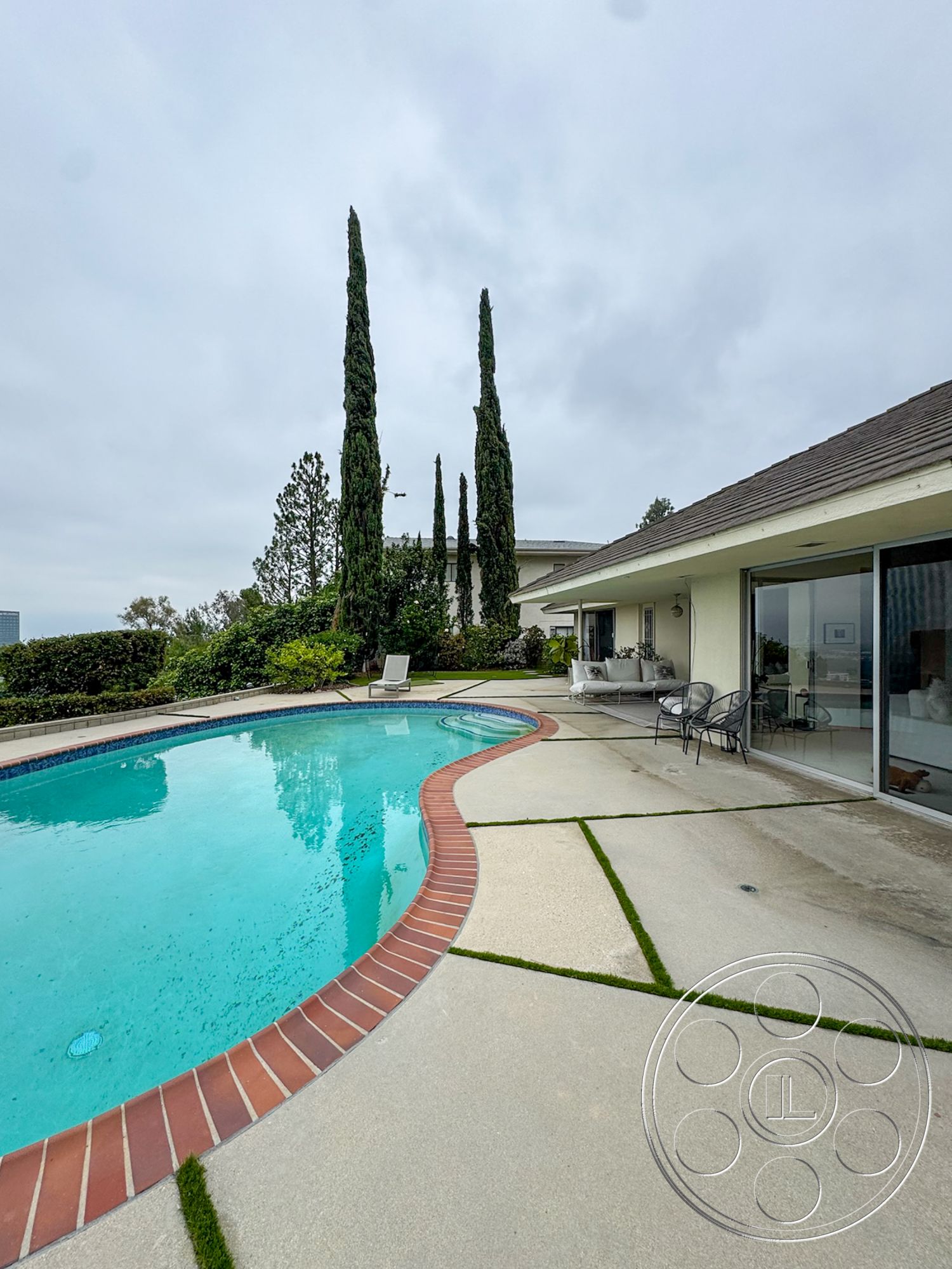 Once Upon Hollywood - glass sliding doors, modern outdoor furniture, urban setting, landscaped backyard, tall cypress trees, rectangular pool, skyline view, concrete pool border, concrete patio floor, stone garden landscaping, wall-mounted garden lights