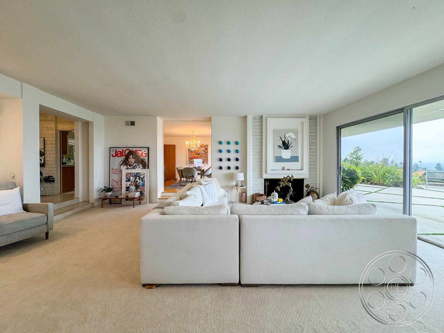 Once Upon Hollywood - minimalist decor, natural light, large glass sliding doors, open floor plan, interior living room, exposed brick fireplace wall, white painted walls, contemporary sectional sofa, built-in shelving unit, neutral carpet flooring, modern accent artwork, dining area with chandelier