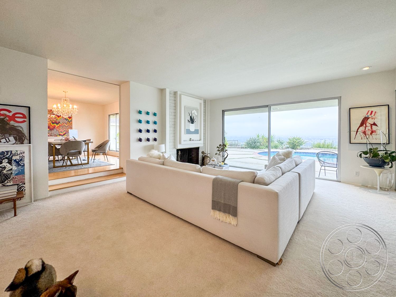 Once Upon Hollywood - textured wall art, open floor plan, glass sliding doors, wooden steps, pool view, floor-to-ceiling windows, urban view, modern chandelier, white sectional sofa, decorative wall accents, contemporary architectural style, neutral painted walls, stone fireplace surround, sunlit living area, carpet living room flooring
