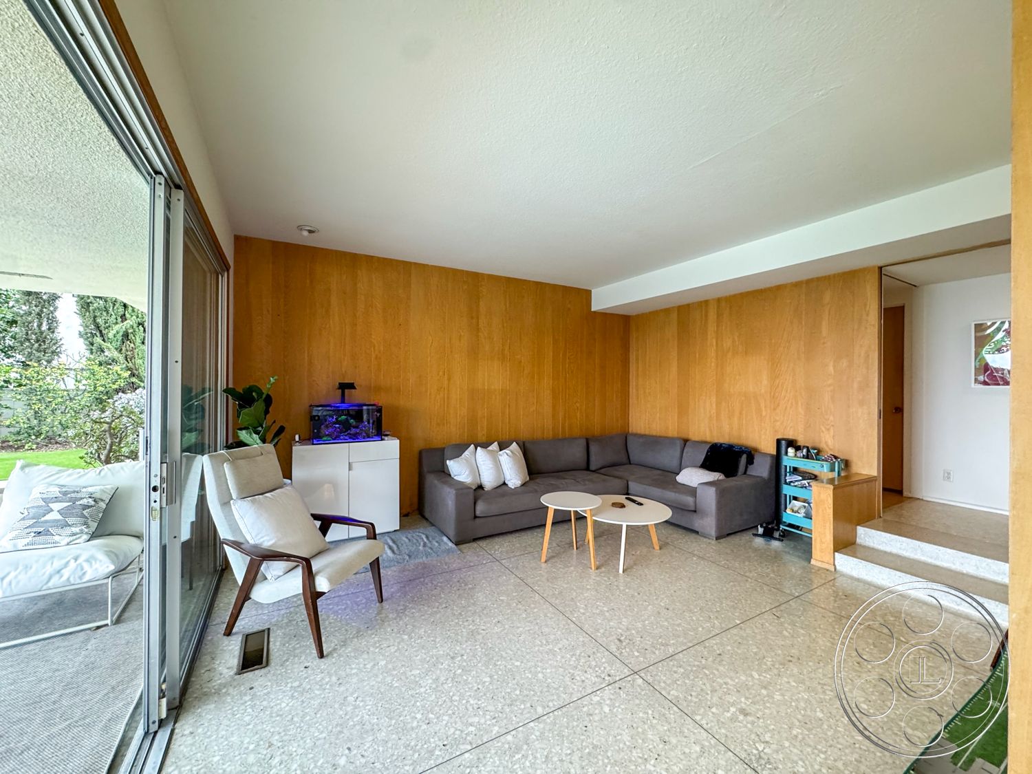 Once Upon Hollywood - round coffee table, polished concrete flooring, living room area, aquarium feature, large sliding glass doors, modern sectional sofa, decorative indoor plants, wood panel accent wall, tiled entry steps