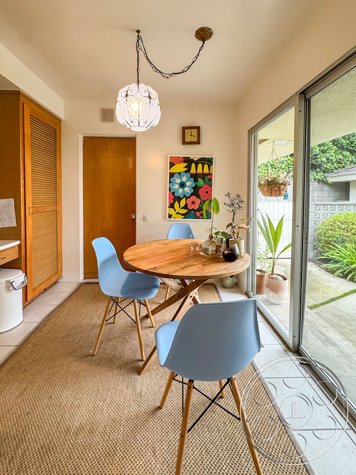 Once Upon Hollywood - natural light, wooden cabinetry, potted plants, wood dining table, sliding glass door, textured wall treatment, tile floor, woven jute area rug, exposed light fixture, painted accent wall, blue molded plastic dining chairs, artwork with floral design, indoor dining area