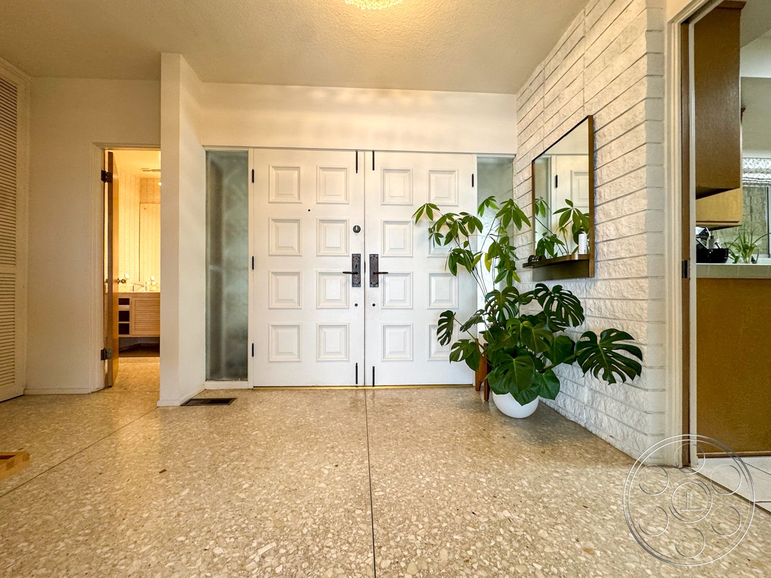 Once Upon Hollywood - terrazzo flooring, open floor plan, modern architectural style, double front doors, exposed brick accent wall, natural light entryway, glass panel sidelights, framed mirror with wood trim, potted houseplants