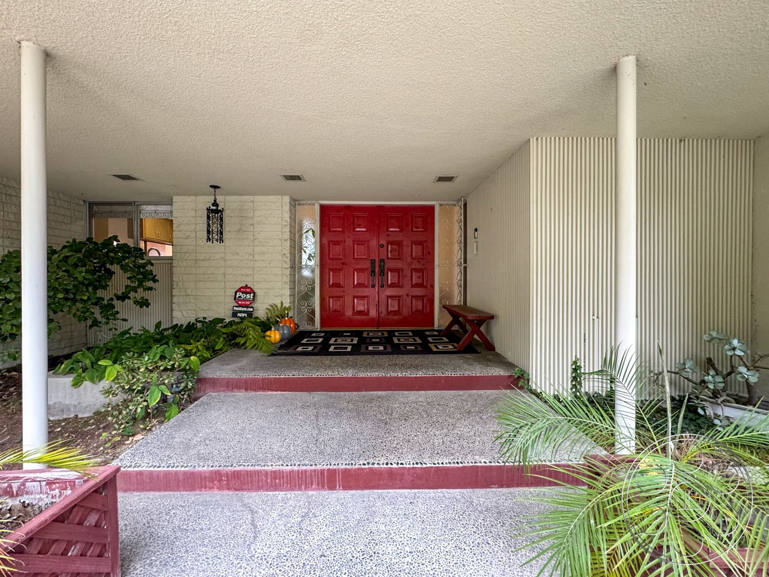 Once Upon Hollywood - exterior, stone accent wall, landscaped greenery, decorative pumpkins, textured ceiling, horizontal wood paneling, open porch area, exposed aggregate concrete steps, hanging lantern light fixture, red double front door, brick planter box, symmetric porch design, black and white geometric entry rug