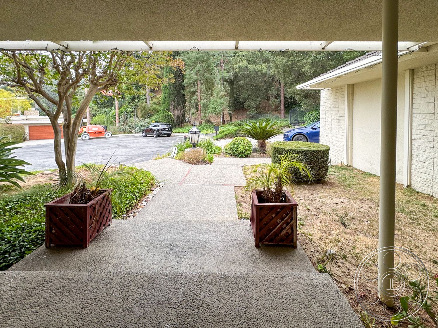 Once Upon Hollywood - exterior, paved driveway, lush greenery, front porch, concrete walkway, pathway lighting, landscaped garden area, natural hillside backdrop, decorative wooden planters, trees and shrubs, stone wall detail, modern home façade