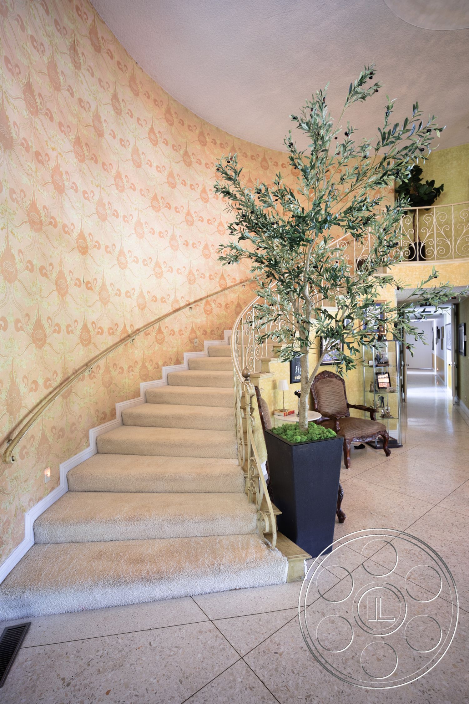 Euphoria - indoor plant, stone flooring, open hallway, textured plaster walls, accent chair, curved staircase, carpeted stairs, decorative wall pattern, arched railing