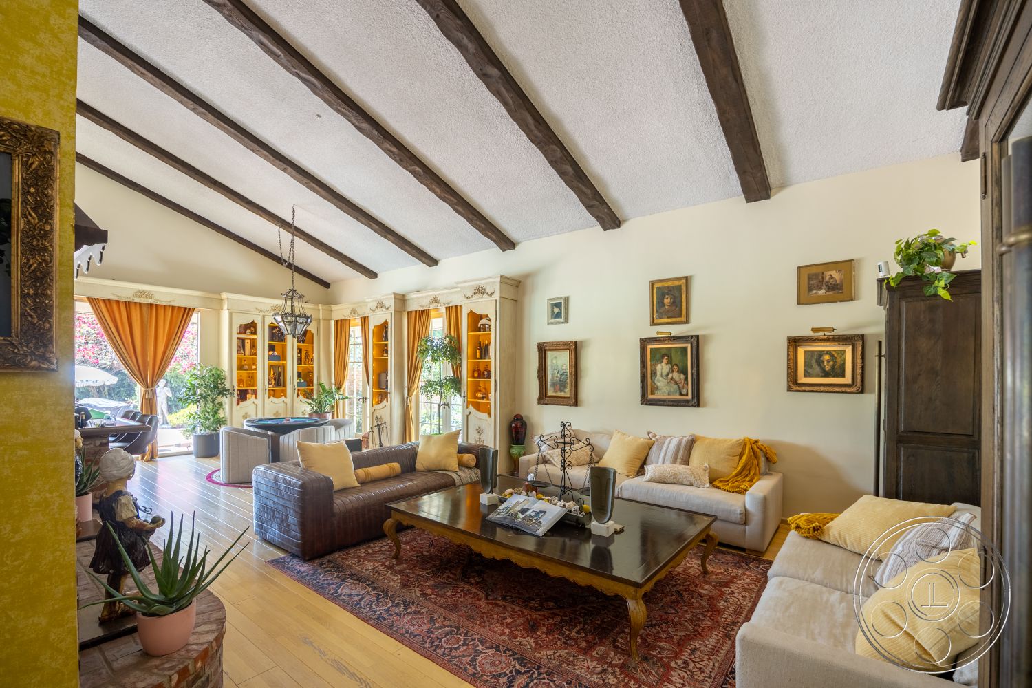 Euphoria - wooden coffee table, textured plaster walls, exposed wood ceiling beams, hardwood living room floors, traditional area rug, built-in shelving units, decorative plant accents, upholstered sectional sofa, framed artwork on walls, curtained window treatments, dark wood frame windows, elegant pendant light fixture, orange drapery panels