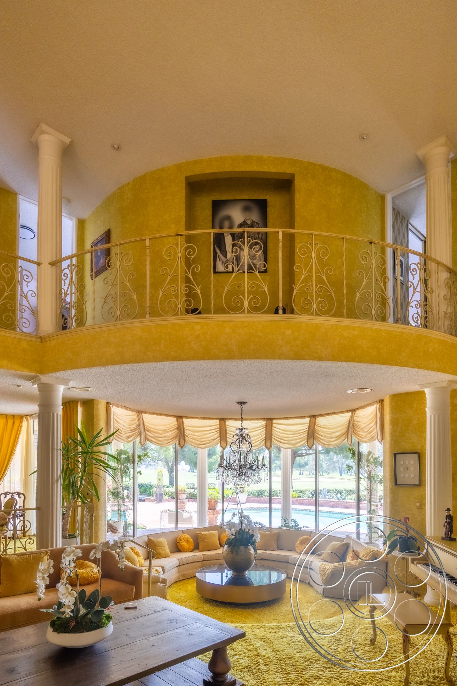 Euphoria - round coffee table, decorative pillows, wooden dining table, plush sectional sofa, decorative wall art, green indoor plants, bright natural lighting, curved architecture, textured plaster walls, iron balcony railing, chandelier lighting fixture, yellow painted walls, large bay windows, exposed column structure, soft yellow area rug