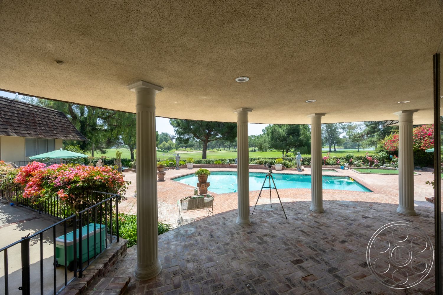 Euphoria - exterior, outdoor seating area, metal railing, rectangular swimming pool, outdoor furniture, shingle roof, brick patio flooring, sunny patio space, green lawn view, surrounding landscaped garden, plaster ceiling, flowering plants in garden beds, decorative outdoor columns, poolside decking, pool area with garden views