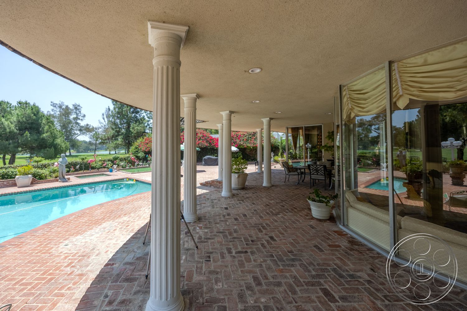 Euphoria - exterior, rectangular swimming pool, outdoor dining area, terracotta planters, poolside seating area, brick patio flooring, glass window walls, stucco ceiling, landscaped garden with flowering plants, columned porch supports