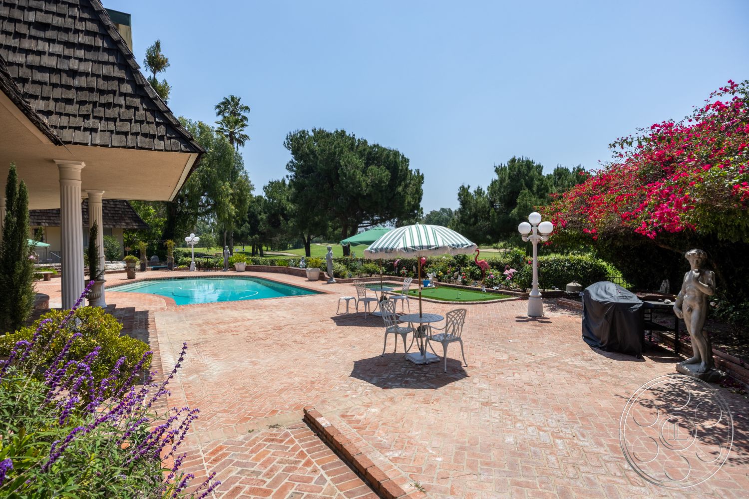 Euphoria - exterior, landscaped garden, potted plants, outdoor grill, bushes, palms, white outdoor furniture, rectangular pool, striped patio umbrella, golf putting green, flowering shrubbery, concrete pool border, brick patio flooring, tile pool deck, exposed columns, sloped shingle roof, decorative garden statue