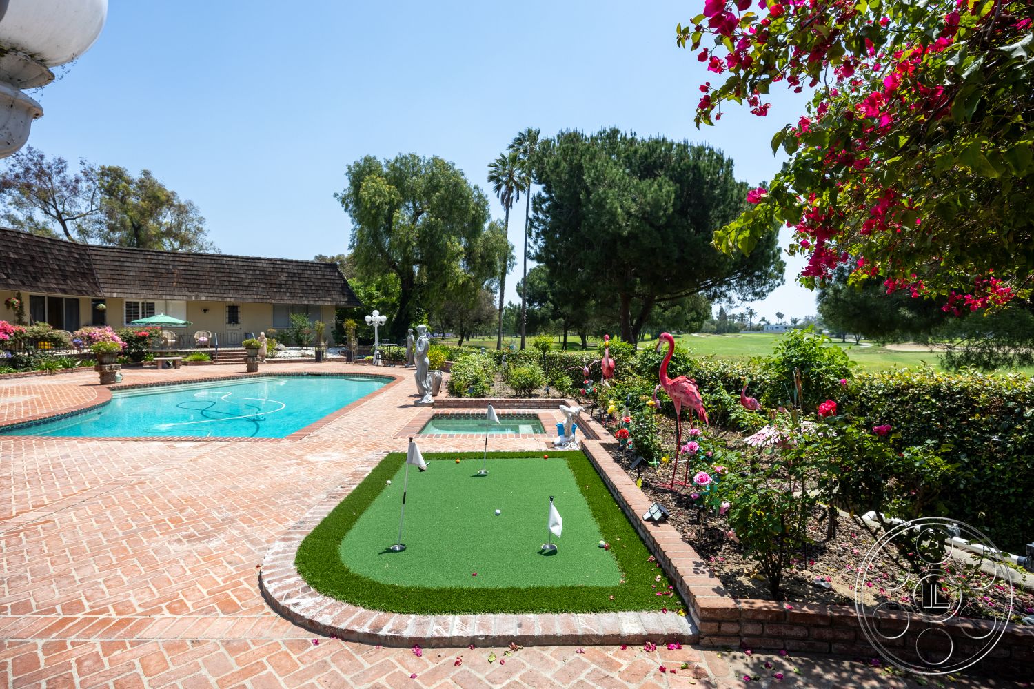 Euphoria - exterior, outdoor seating area, single-story home, flowering shrubs, brick pool deck, curved pool shape, landscaped garden area, brick patio flooring, wood shingle roof, golf course view, tile swimming pool, artificial turf putting green, decorative garden flamingos